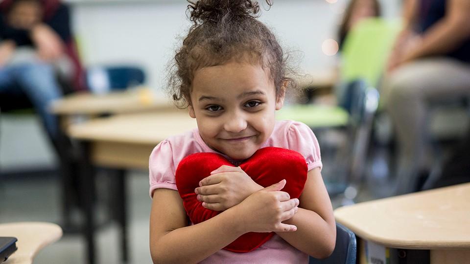 Child hugging heart-shaped pillow