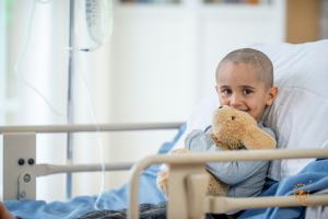 a toddler in a hospital bed holding a teddy bear