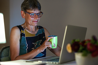 A woman holding a mug and looking at a laptop screen