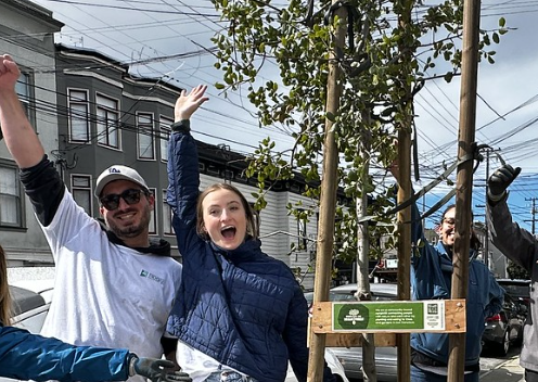 two volunteers raising hands in glee, having just planted a tree
