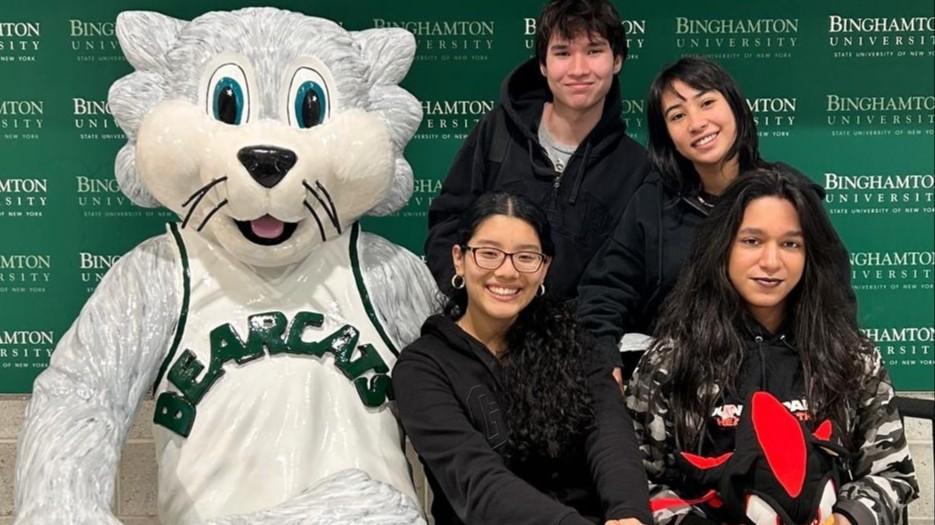 High school students pose next to a college mascot during a campus visit.