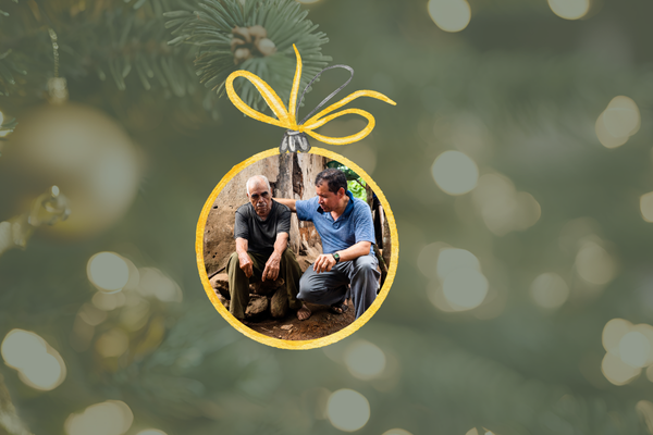 An image of a Christmas ornament featuring a man with his arm around an elderly man, praying for him.  