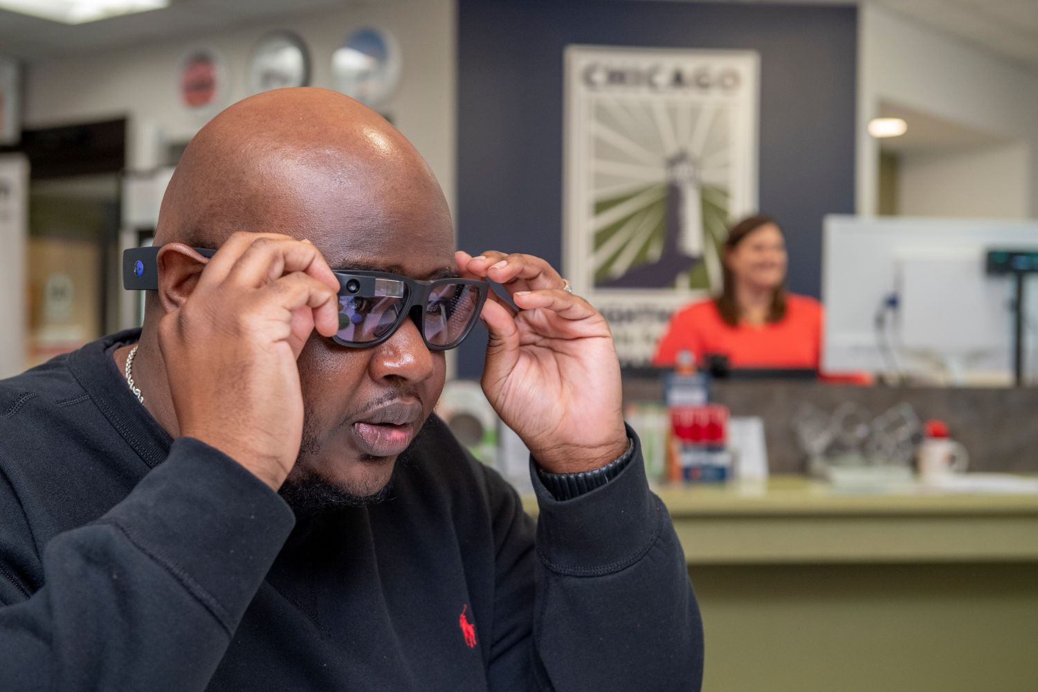 A man putting a pair of glasses on his face at an optician's office with a staff member visible in the background.