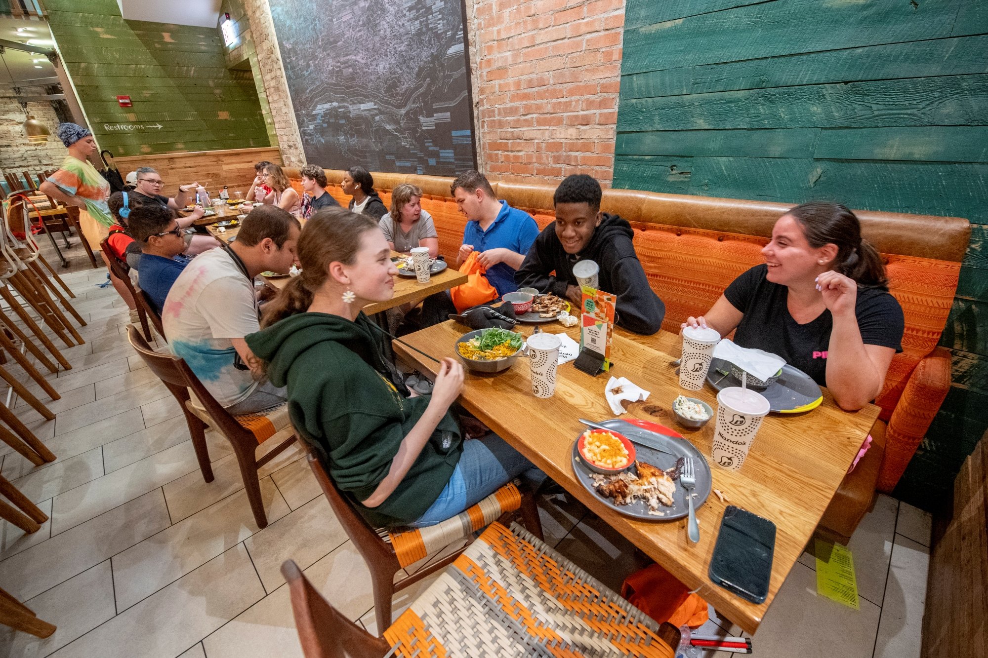 A group of youth who are blind or visually impaired sit together at a restaurant table, chatting with food in front of them.