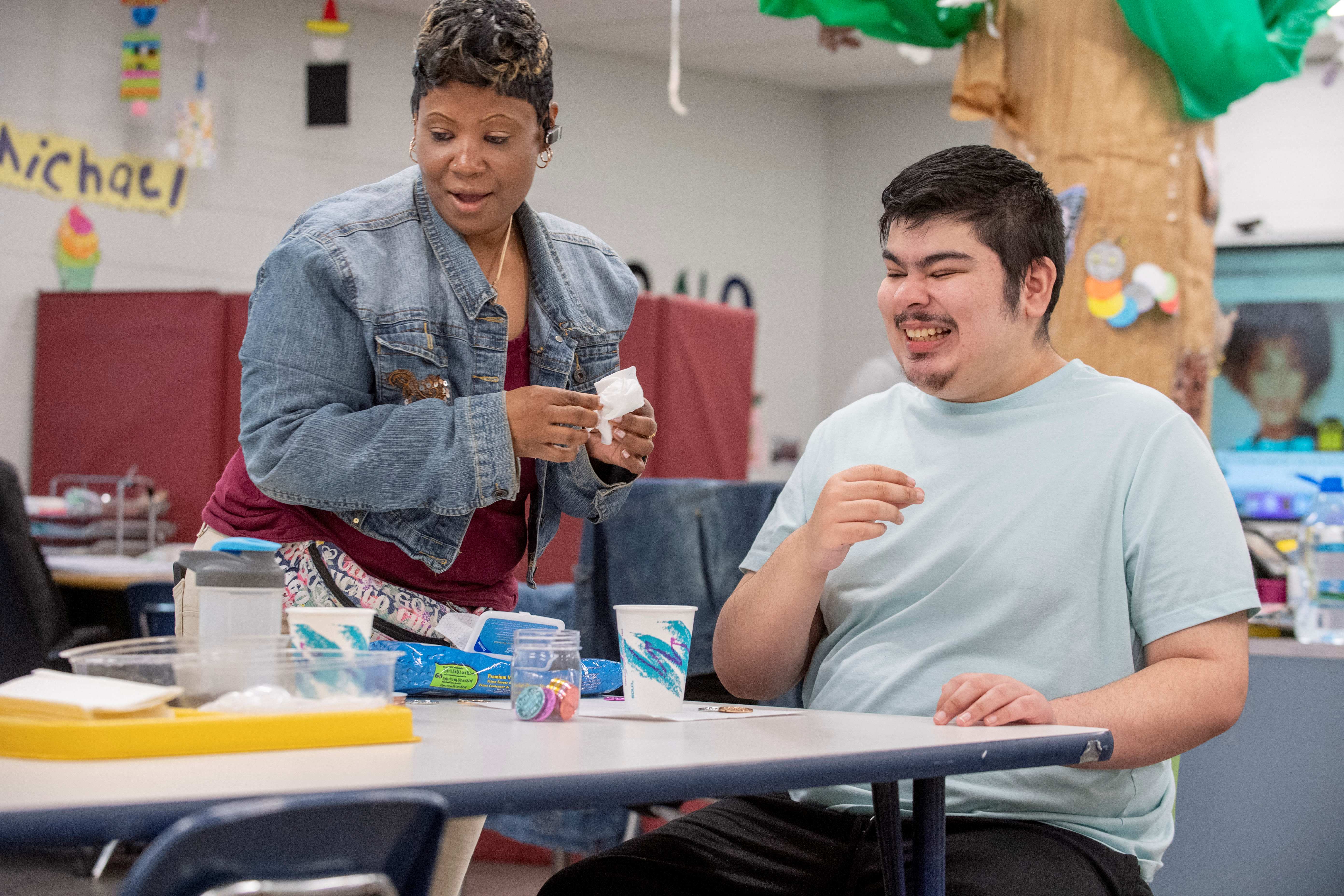 An older student smiles as a teacher helps him with an art project.