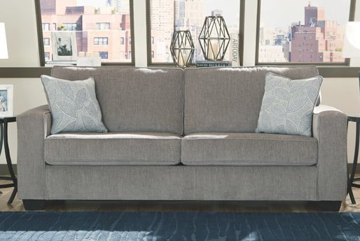 Light grey sofa with two light blue patterned pillows on it in front of a window. 