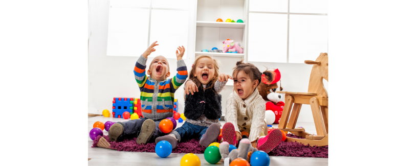 3 children sitting on floor of playroom laughing