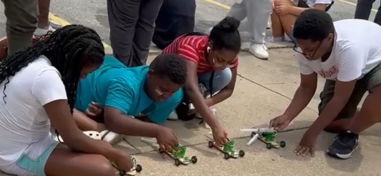 group of four students on a sidewalk outside setting their Cruiser projects up to race.