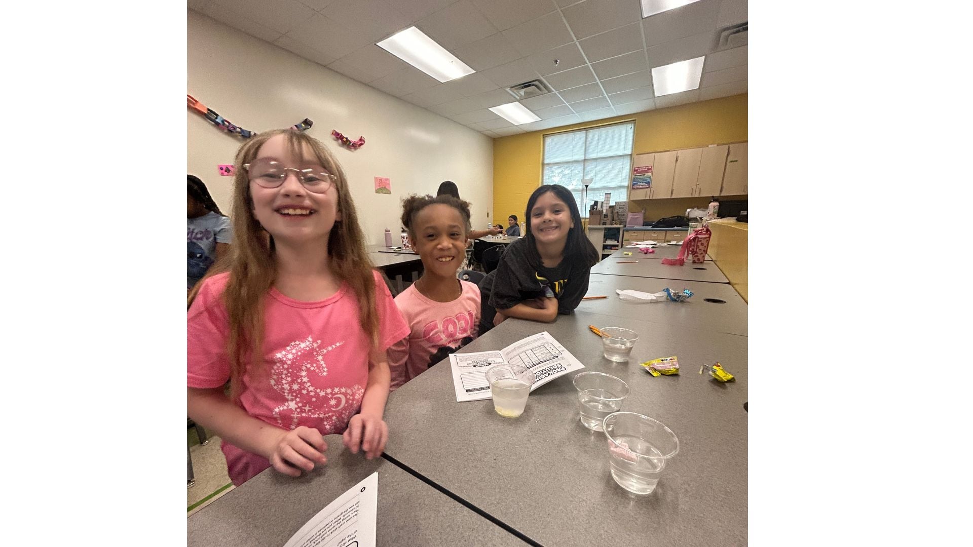 3 young girls smiling while doing a STEM experiment in a lab