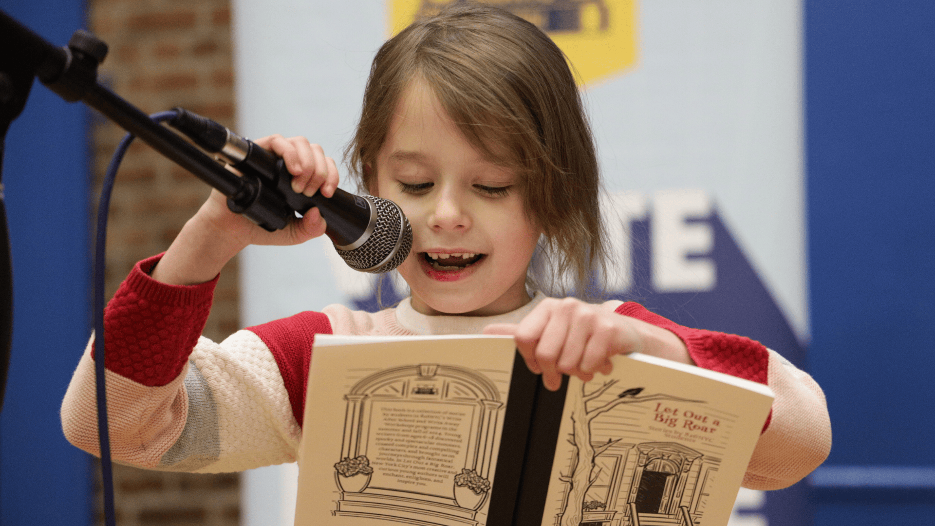 One 826NYC student reads their piece aloud from a chapbook at a book release party into a microphone.
