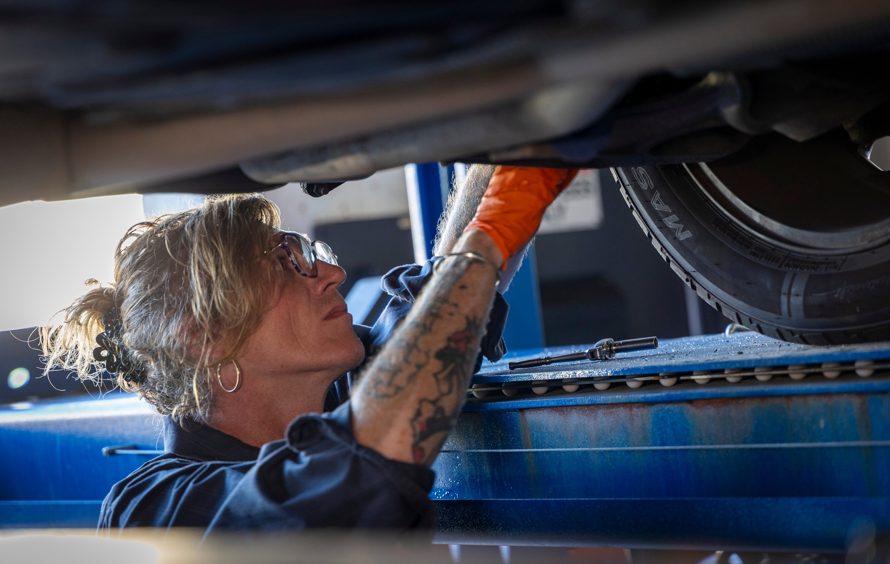 A technician at The Lift Garage standing underneath a car inspecting a component for damage, leaks, or other problems.