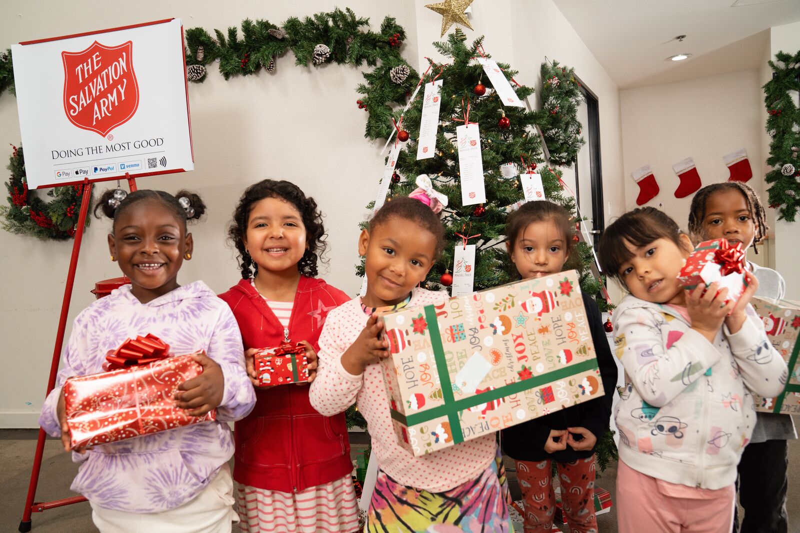 A group of girls smiling with presents from the Salvation Army in front of a Christmas tree.