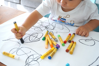 A toddler scribbles at a table with his many colorful crayons.
