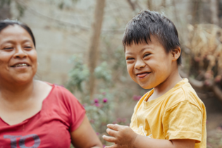 A boy with Down's Syndrome in LWB's Guatemala Medical Program smiles with his tongue out. His therapist sits with him as they laugh together.