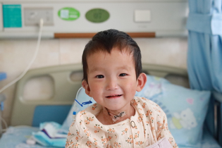A young Chinese girl in LWB's cardiac program sits on a hospital bed. She smiles sweetly at the camera.
