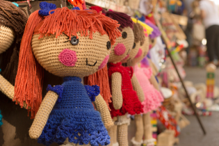 Crocheted dolls are lined up at an outdoor market.