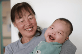 A Chinese mother is holding her baby son with cleft needs while they both laugh together.