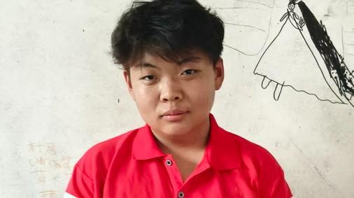 Hector stands in front of a wall with a drawing of a girl in a long dress done in black crayon.  He wears a red shirt and looks directly into the camera.