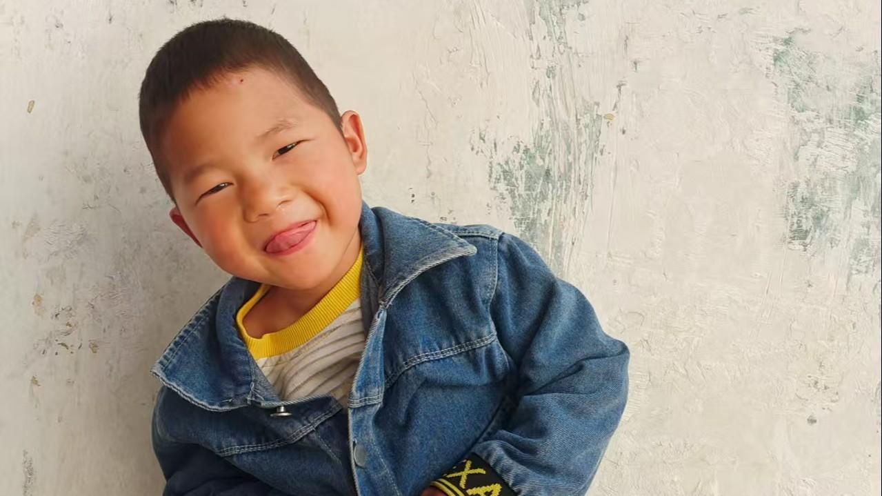 Arthur smiles at the camera. He wears a striped striped shirt with yellow trim and a denim jacket.