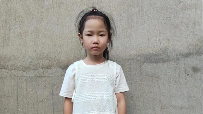 Kaylynn wears a cream shirt and vest in front of a concrete wall.