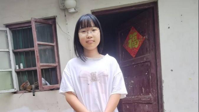 Harriet stands in front of a door. She is wearing a white shirt and glasses.  Her black hair hangs to her shoulders with bangs cut straight across her forehead.