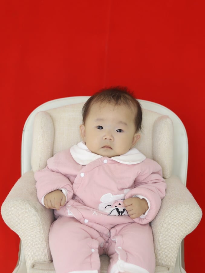 Jennie sits in a little cream colored chair looking straight at the camera.  
