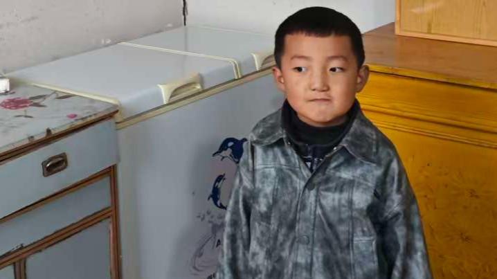 Tom stands in front of a cabinet in a grey flannel.  He looks off to the left of the camera.