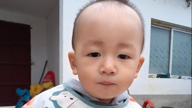 Malachi stands in front of his home in a grey hoodie with a white and blue bib on.  
