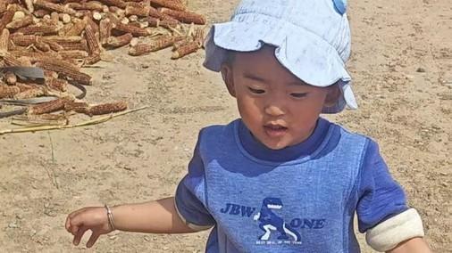 Nathaniel is wearing a blue shirt with a dinosaur and a white hat. He is running across a worn dirt lot.