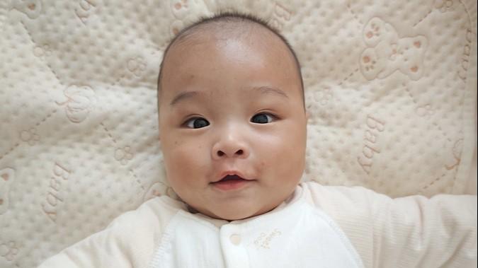Lincoln looks at the camera with bright eyes and a smile.  He is wearing cream pajamas and is laying on a cream blanket.