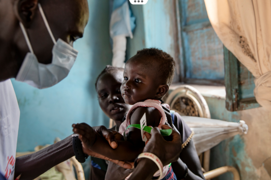 Mother holds her baby as a member of Doctors Without Borders/ Médecins Sans Frontières staff measures the child’s level of nutrition. Image is from South Sudan.
