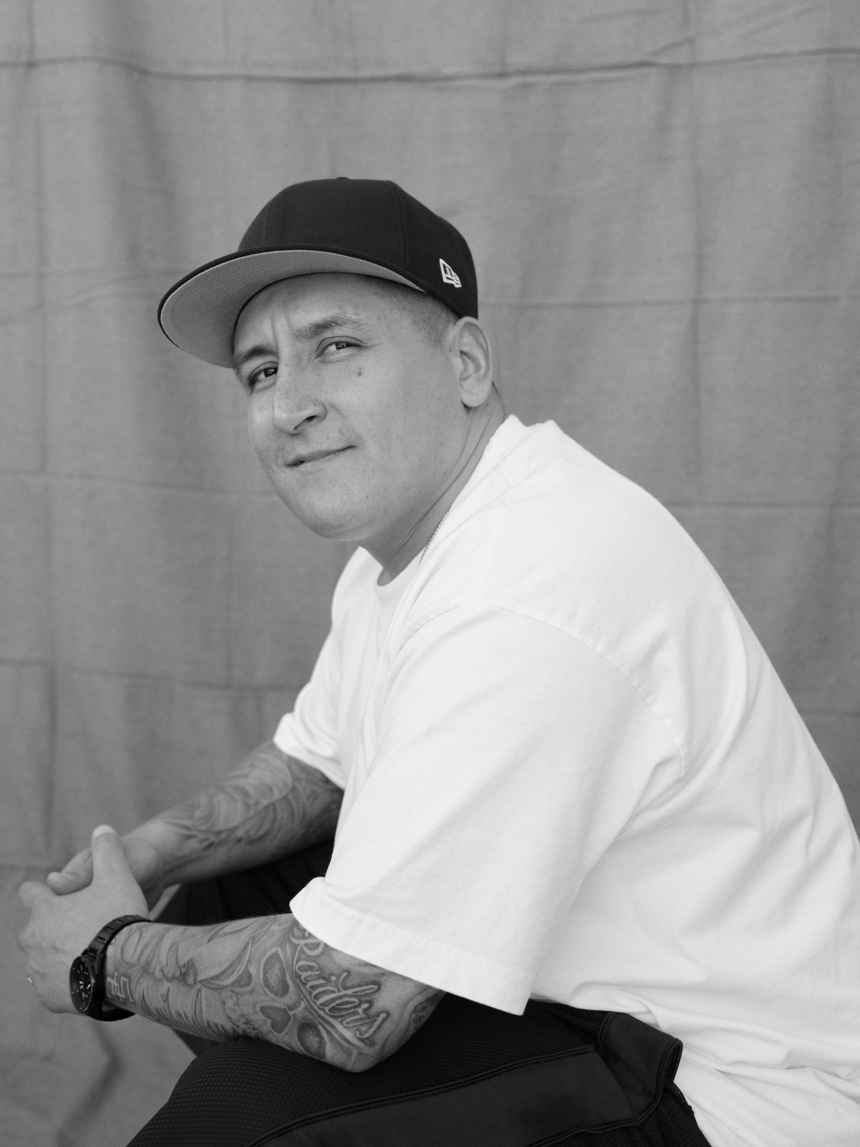Latino man wearing a white shirt looks over his shoulder and smiles at the camera.