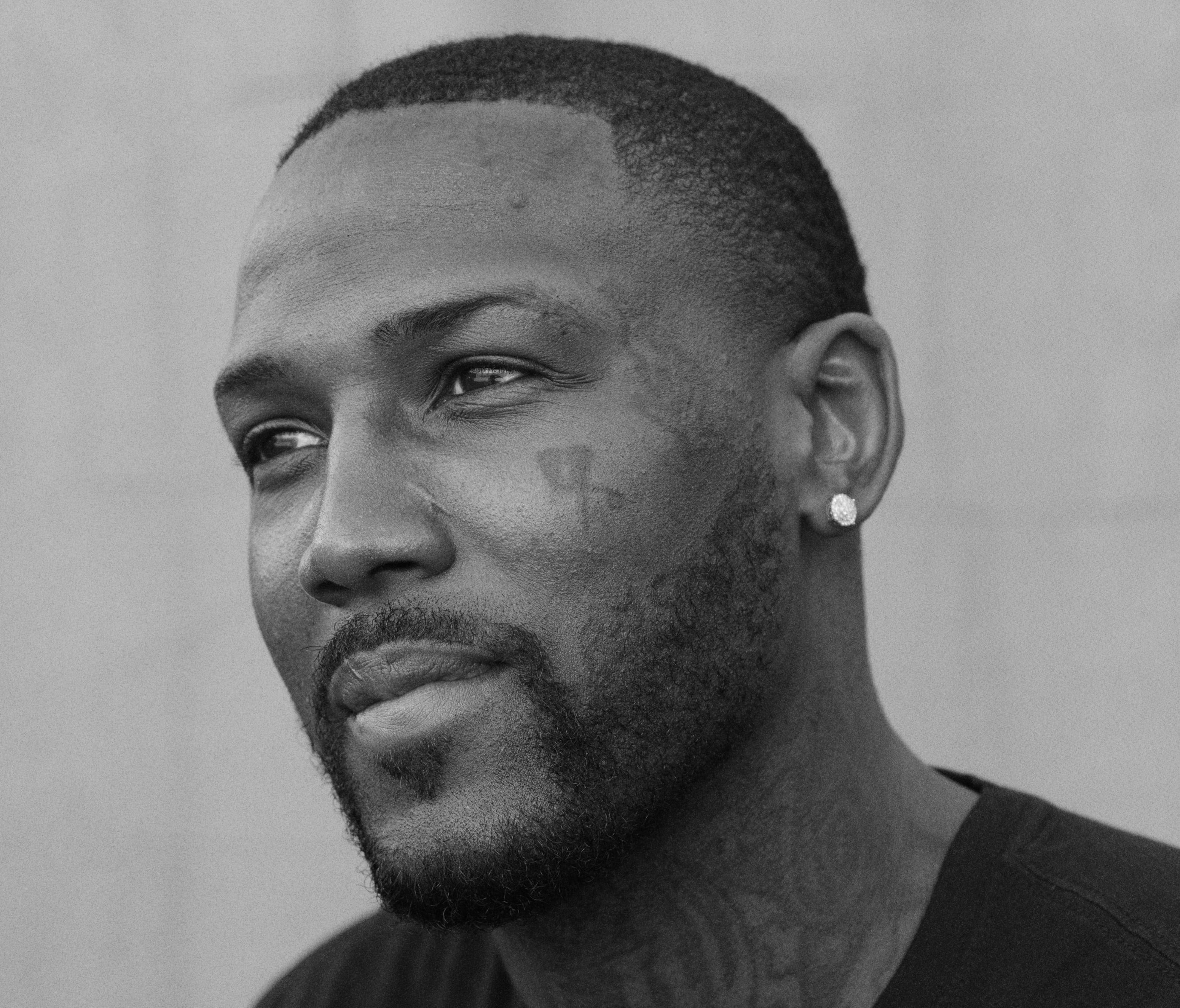 Black man with a small face tatoo, goatee and a fade looks wistfully to the side.