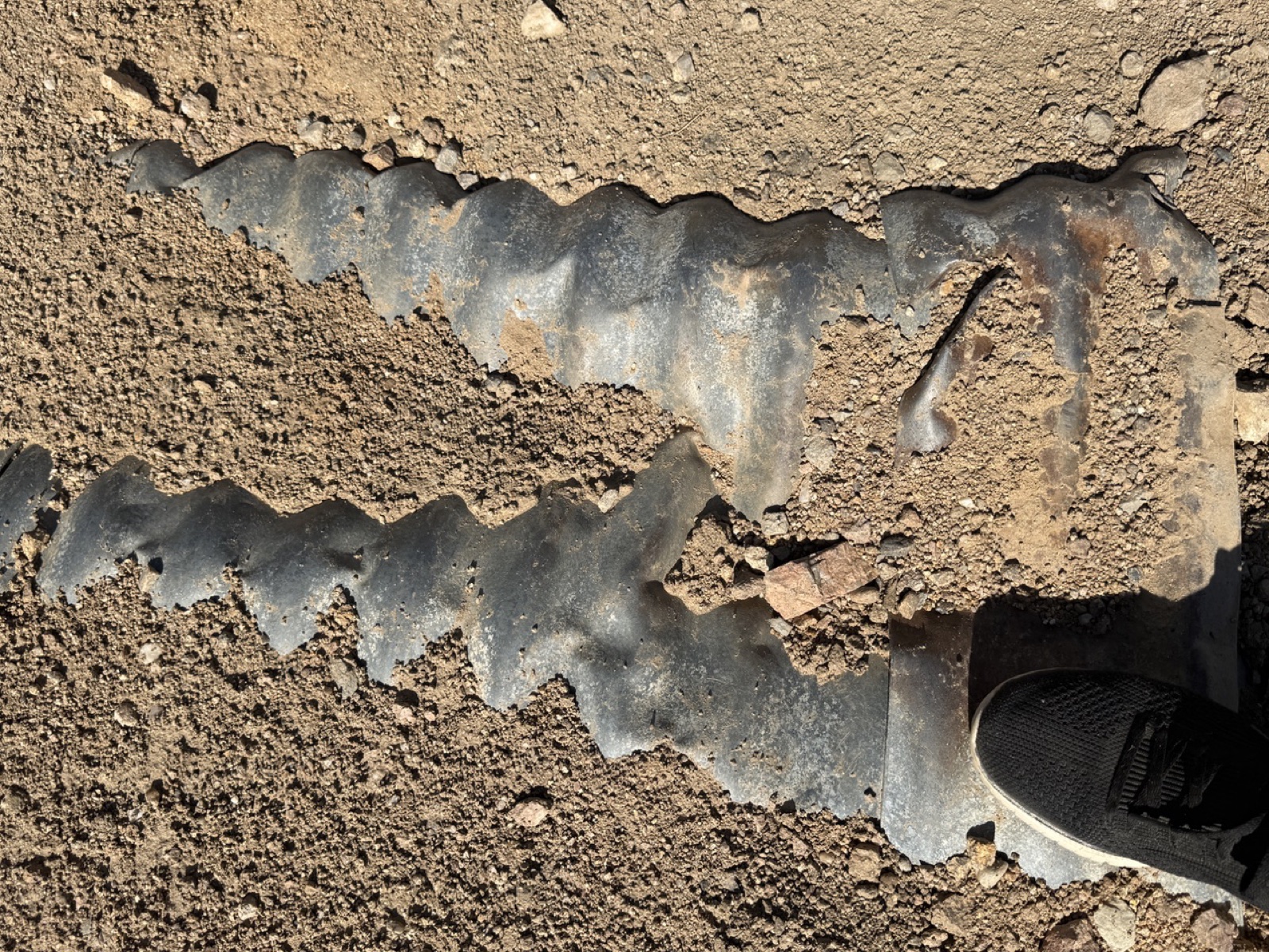 A crushed steel culvert worn through the road surface