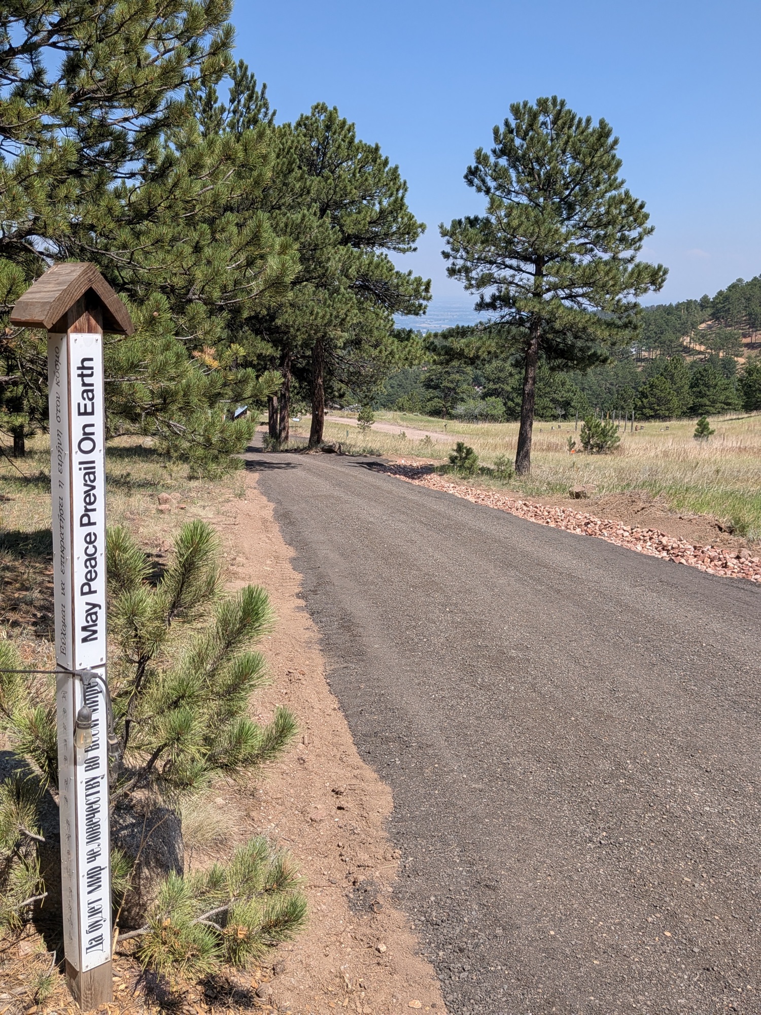 The rebuilt road descending past a white Peace Pole reading May Peace Prevail On Earth, with the valley beyond