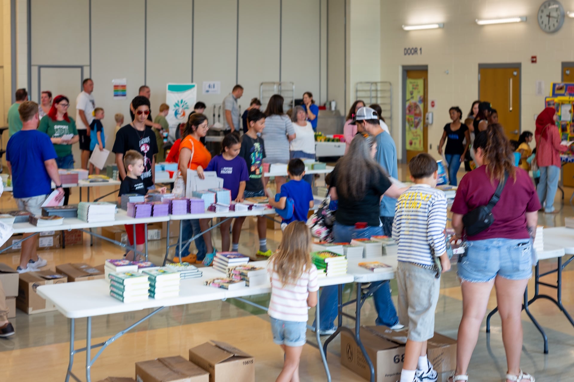 A room of kids and their parents picking out books from tables of free books.